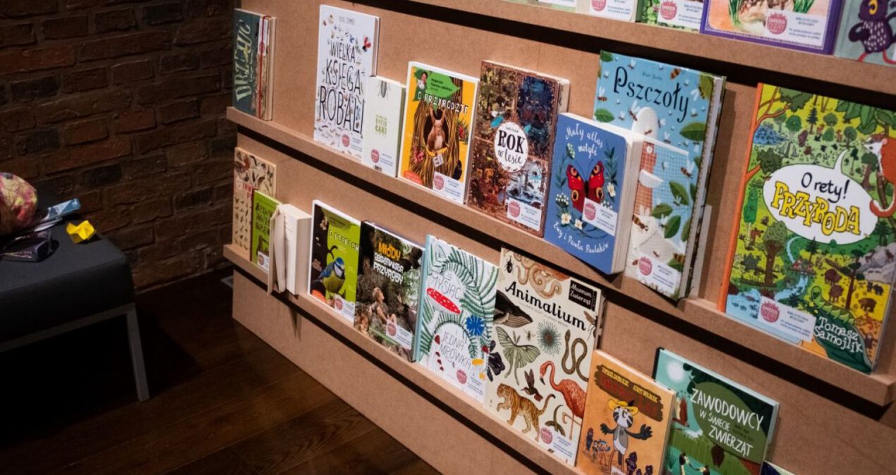 Na drewnianym regale umieszczone są książki dla dzieci o tematyce przyrodniczej. Mają kolorowe okładki.