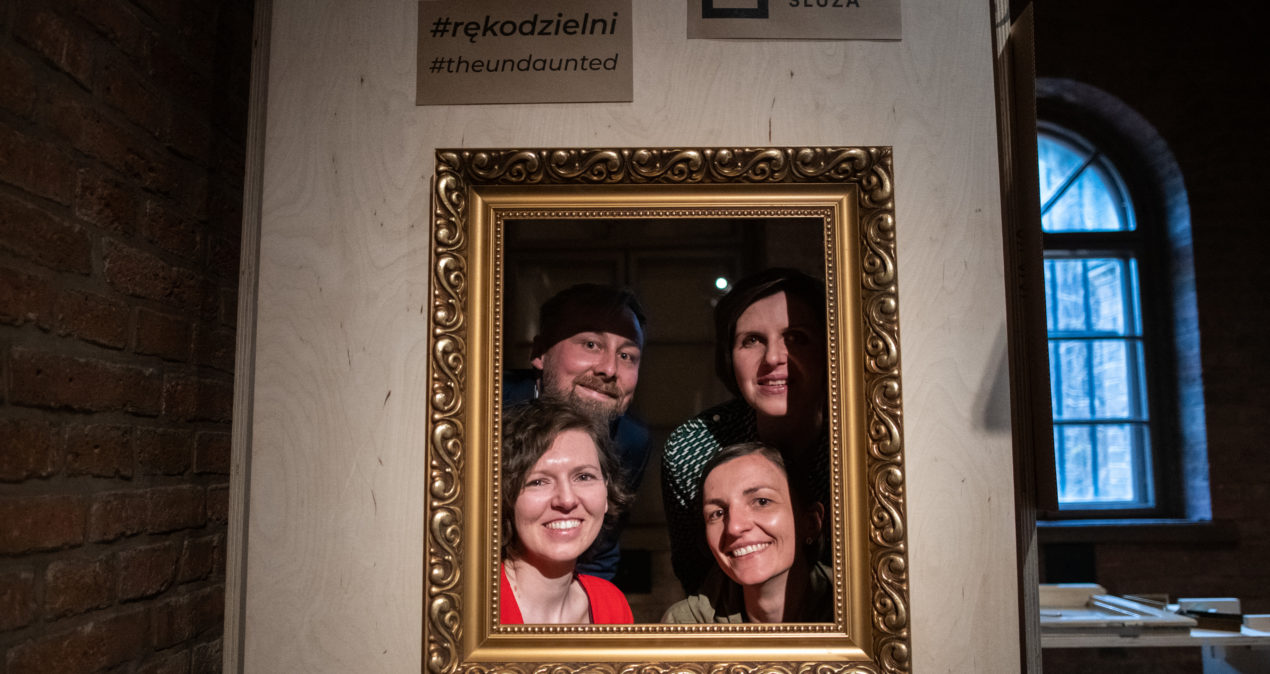 Cztery osoby z zespołu kuratorskiego wystawy widoczne przez ramę obrazu, która jest jednym z nośników na wystawie.