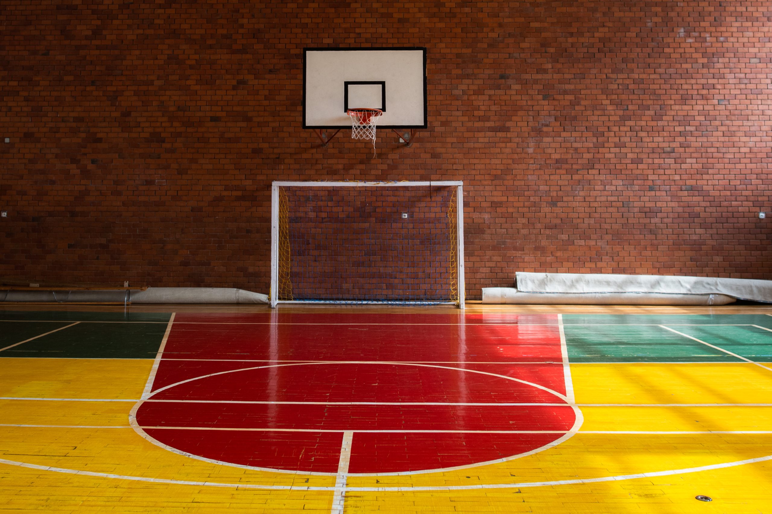 Wnętrze sali gimnastycznej, widok na bramkę do piłki nożnej, nad nią na ceglanej ścianie zamontowany kosz do gry w koszykówkę