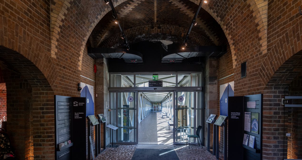 Holl galerii - wyłożone kamieniami przejście, a po bokach standy informacyjne
