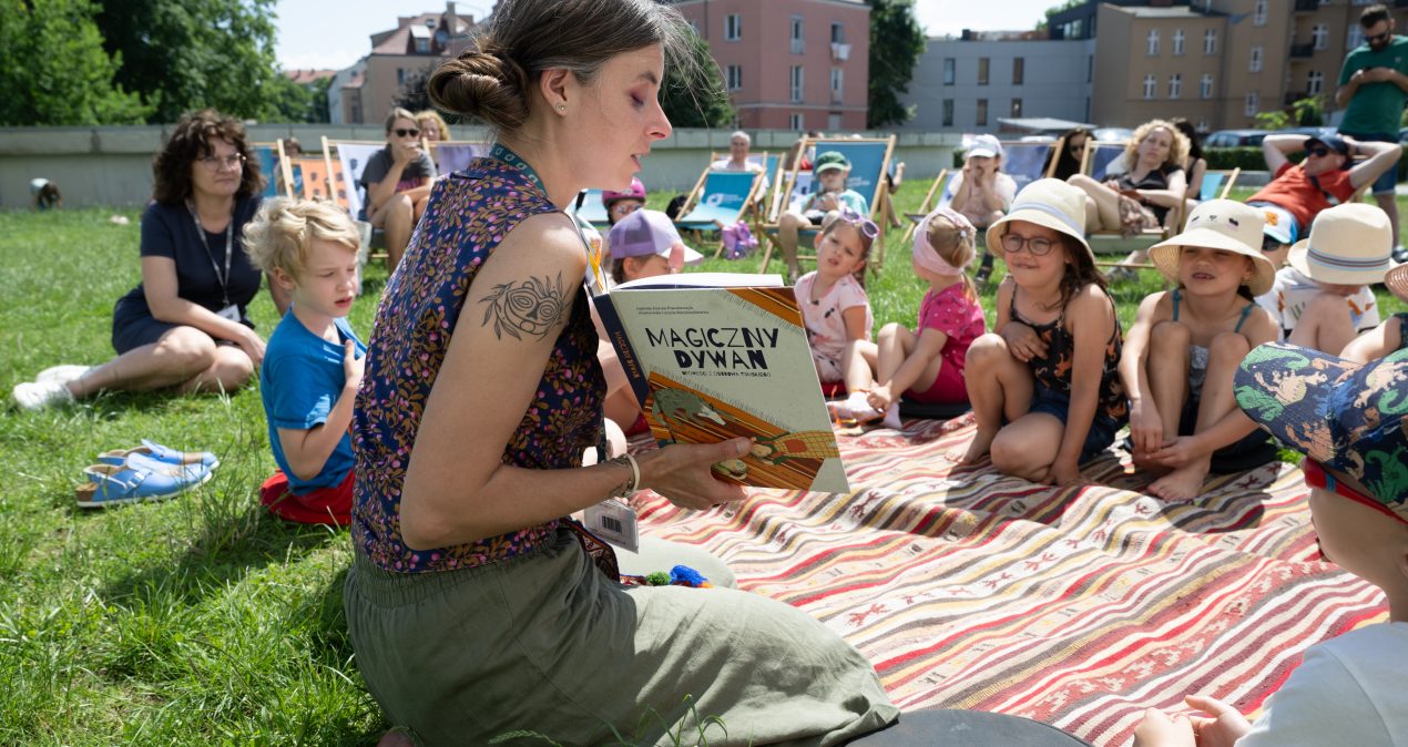 Siedzące na dywanie dzieci słuchają kobiety czytającej książkę
