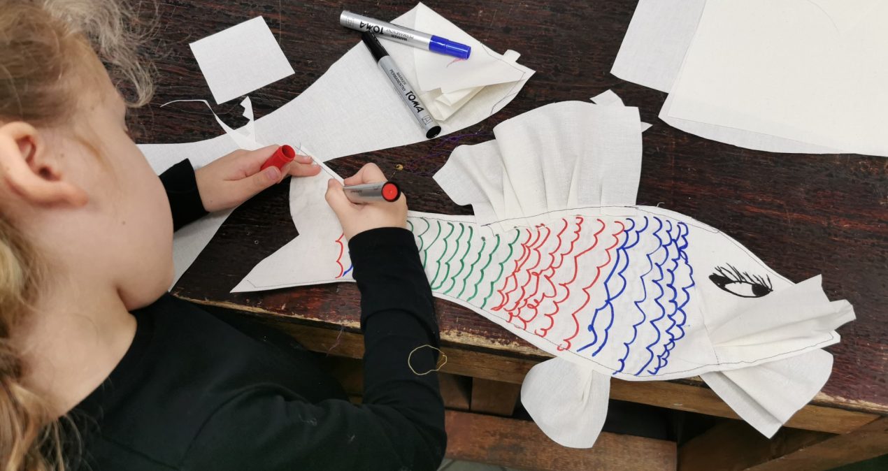 Dziewczynka dekoruje pisakiem ozdobę w kształcie ryby