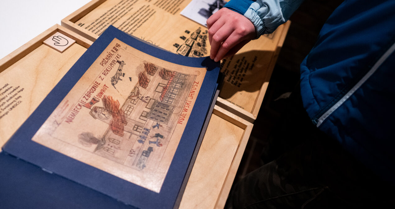 Osoba przegląda album z rysunkami dziecięcymi dotyczącymi wspomnień wojennych