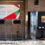 Przestrzeń galerii. Stand z plakatem i plansza z opisem wystawy.